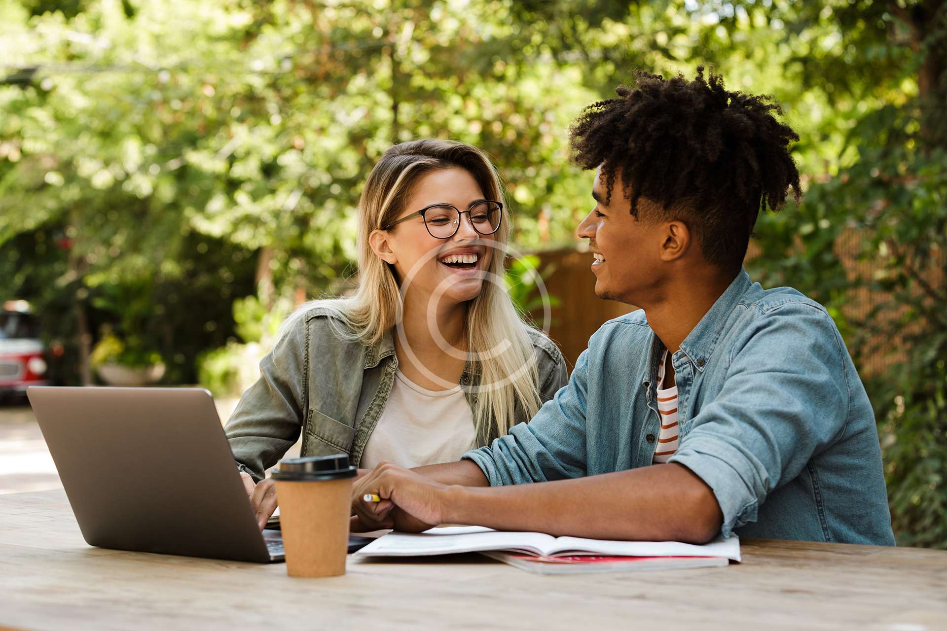 image-17-copyright.jpg Positive young multiethnic couple spending time together at the park, studying while sitting at the table with laptop
